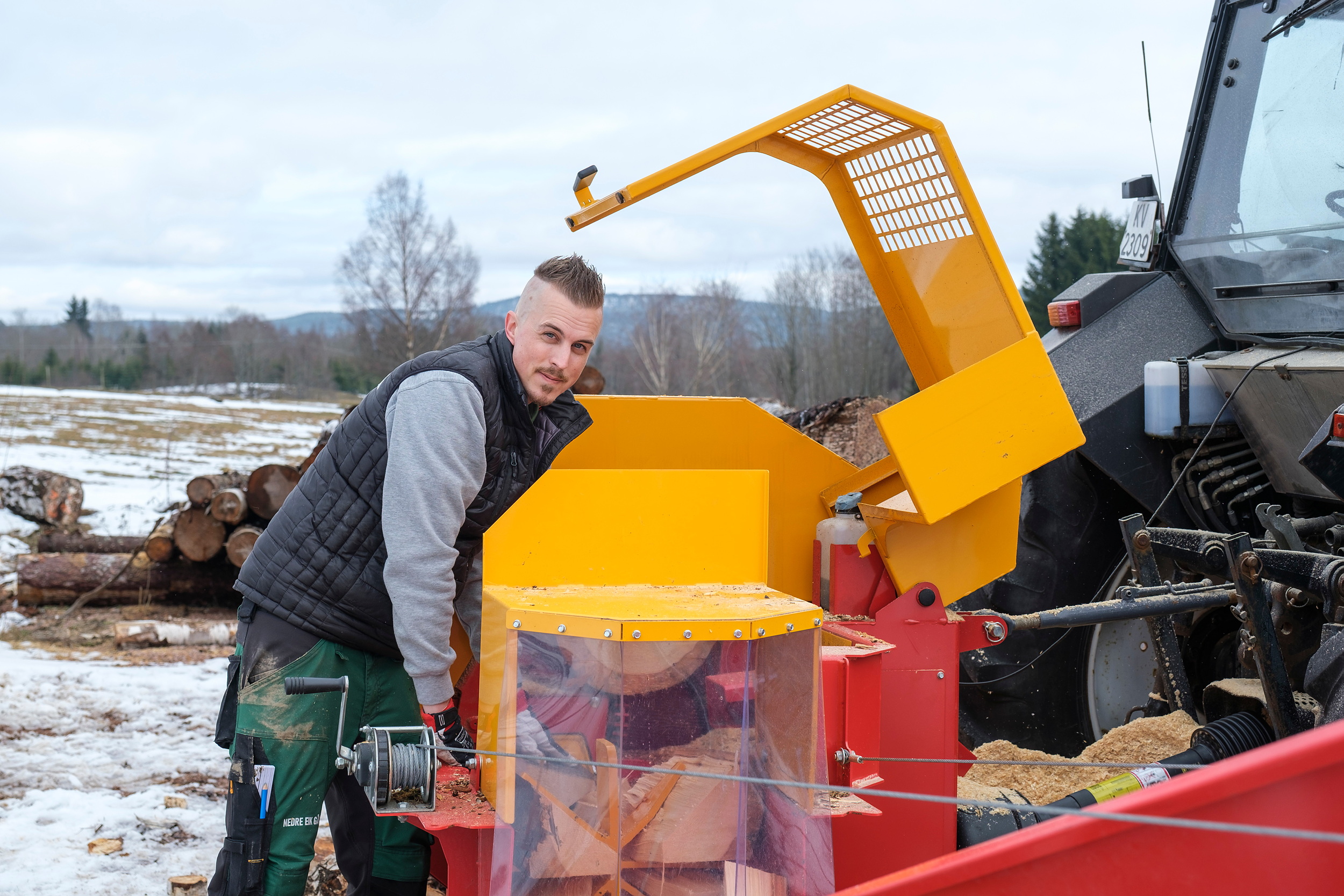 En mann står og jobber med ved ved en traktor